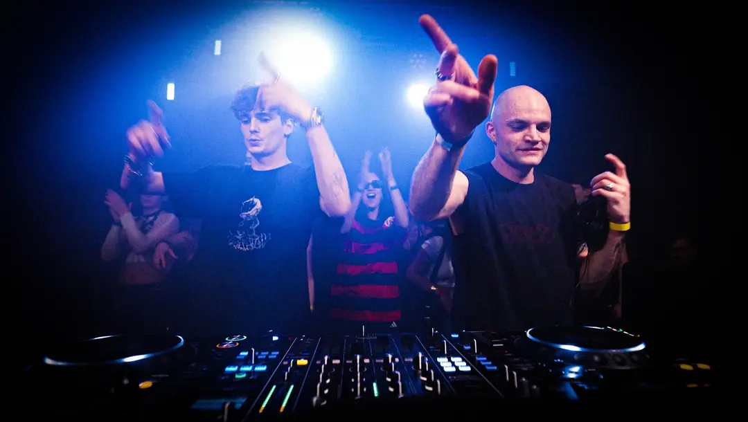 Two DJs with hands raised behind the decks at a CAVE 28 night